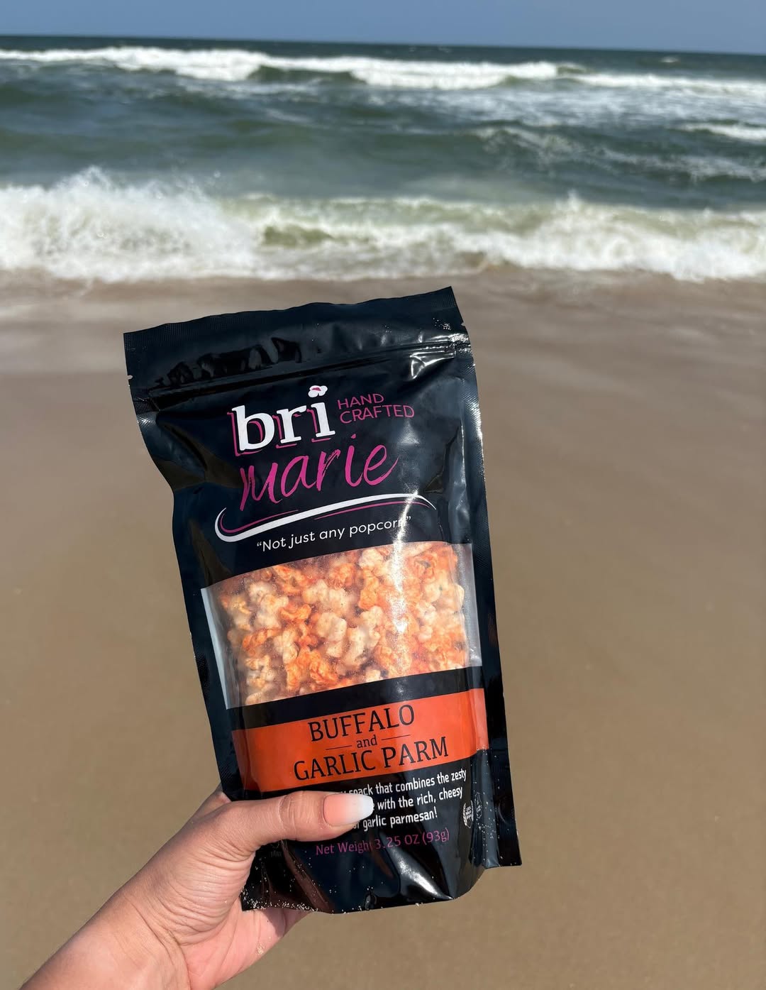 Bri Marie Buffalo and Garlic Parm popcorn held in hand on a beach.