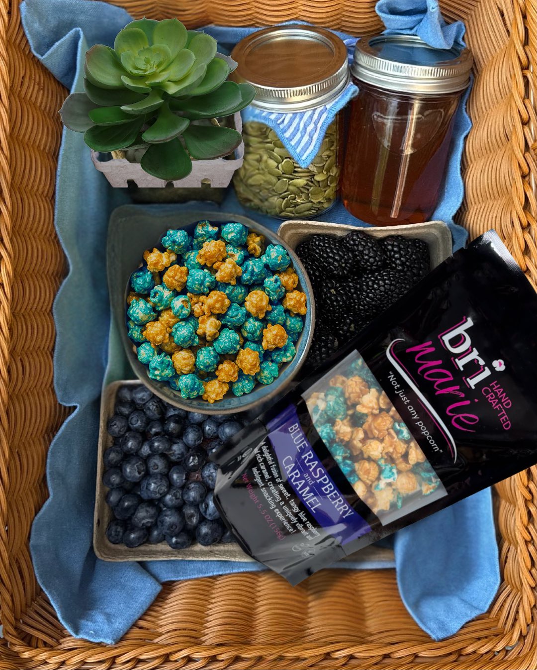Blue raspberry and caramel flavored gourmet popcorn by Bri Marie displayed in a basket with pumpkin seeds, honey, and fresh blueberries.