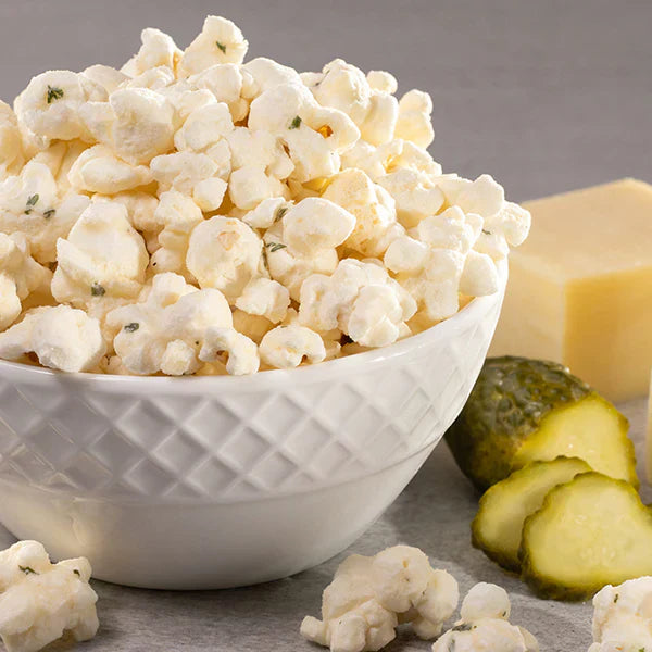 Bri Marie Dill-icious popcorn in a bowl with dill pickles and cheese on the side.