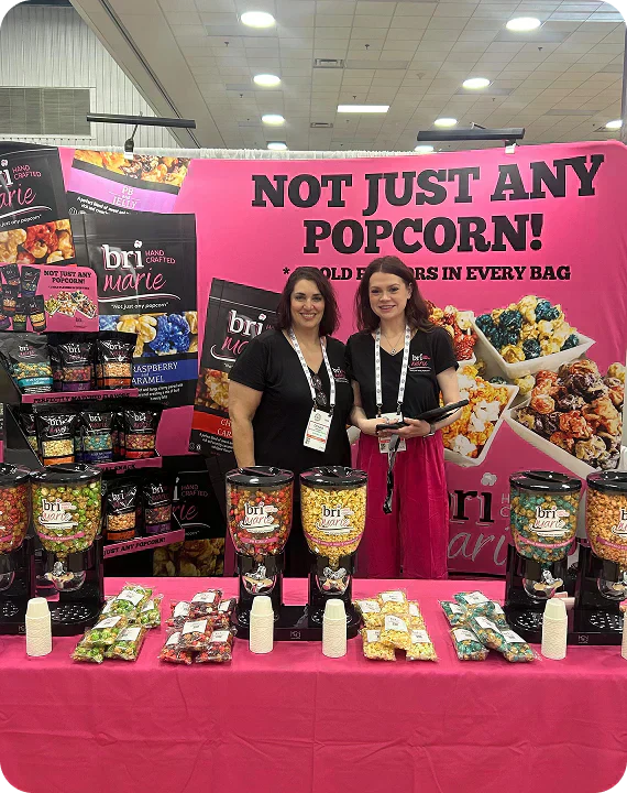 Bri Marie team showcasing colorful gourmet popcorn flavors at a branded trade show booth.