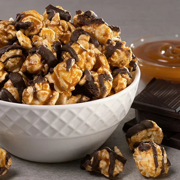 Bri Marie Popcorn caramel popcorn drizzled with dark chocolate, served in a white bowl with chocolate pieces nearby.