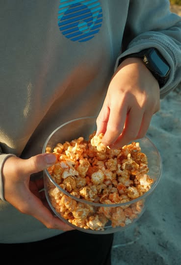Hand reaching into a bowl of Bri Marie’s popcorn while traveling on a road trip