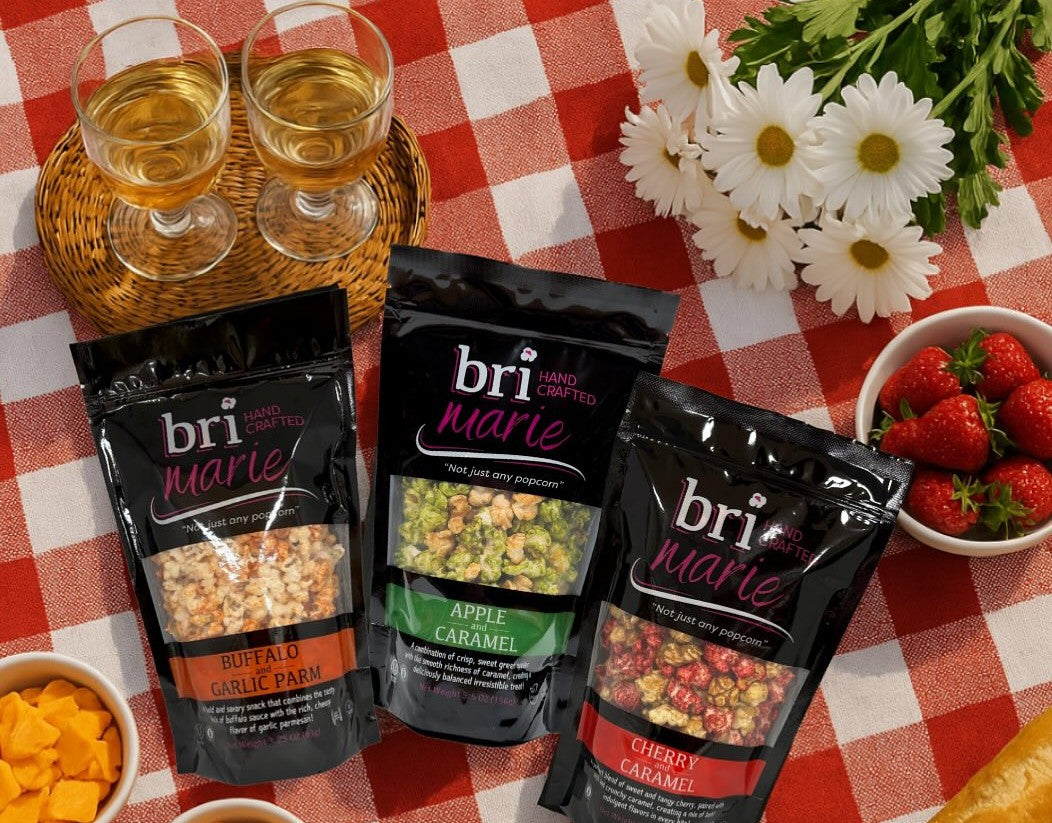 Flatlay shot of three fun flavors of Bri Marie hand-crafted popcorn on a picnic mat.